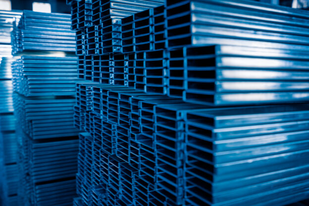 Vigas laminadas de aço empilhadas em estoque, utilizadas em diferentes aplicações industriais e estruturais.